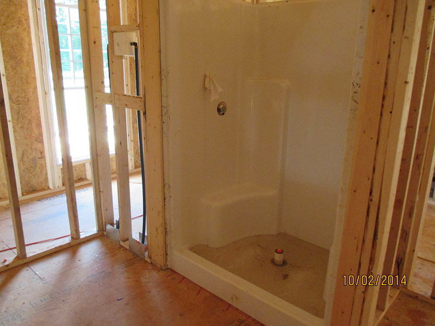 Walk-in shower with glass enclosure, white tile walls, chrome fixtures, and adjacent soaking tub with red candle; bathroom features large window and light-colored flooring