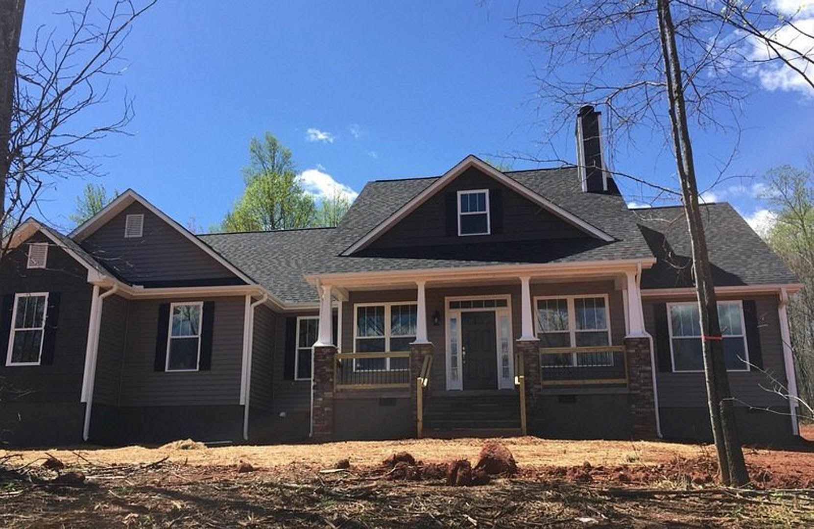 Two-story home with white siding, black front door with glass panes, covered porch, white-framed windows, dirt yard, mature trees, tree trunk wrapped with red tape