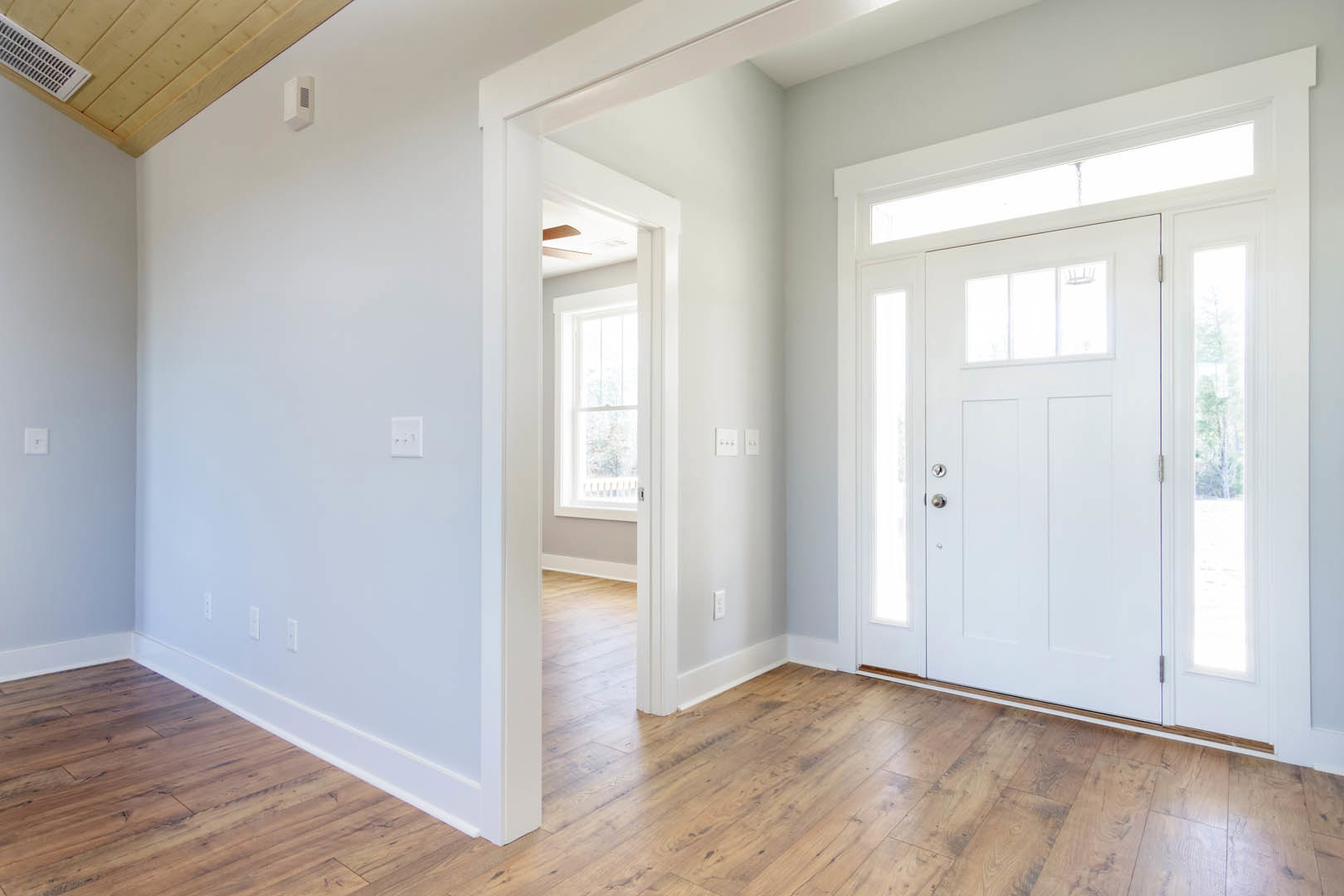 Hallway with white paneled doors, wood laminate flooring, white baseboards, ceiling vent, and a three-button wall switch on a white plaster wall