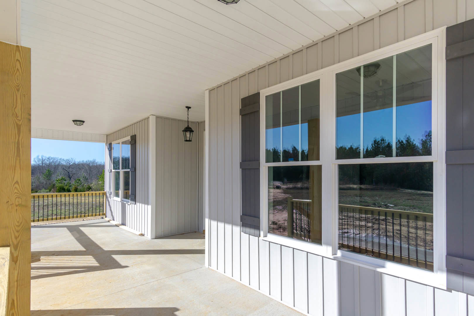 White siding exterior with multiple windows, black metal porch lamp, wooden fence in foreground, tree branches partially visible