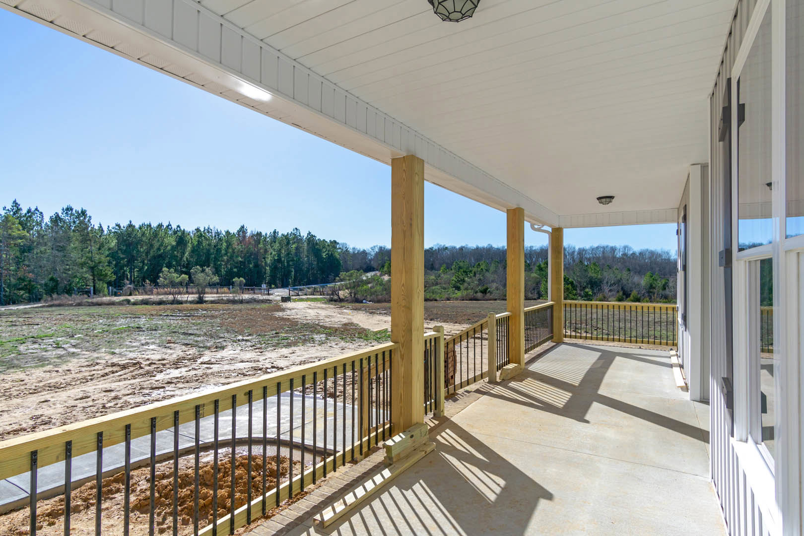 Spacious deck with wooden railing and metal bars, white roof overhead featuring a ceiling light, fenced perimeter, and leafy trees in the background.