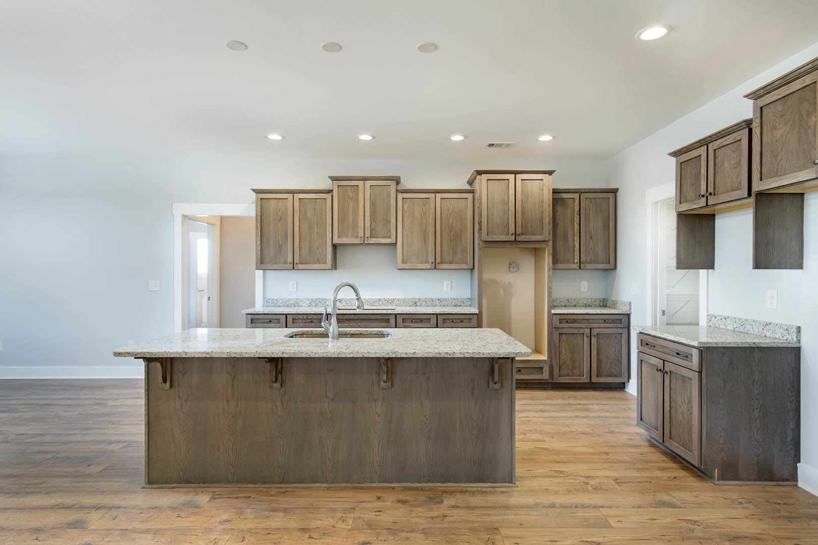 Spacious kitchen featuring a large marble-topped island with built-in sink, wooden cabinetry, tile backsplash, and granite countertops