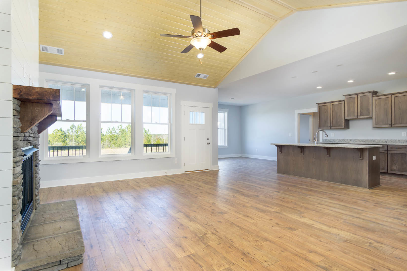 Open kitchen with hardwood flooring, wooden cabinets, ceiling fan with light, white door featuring window, and countertop with built-in sink.