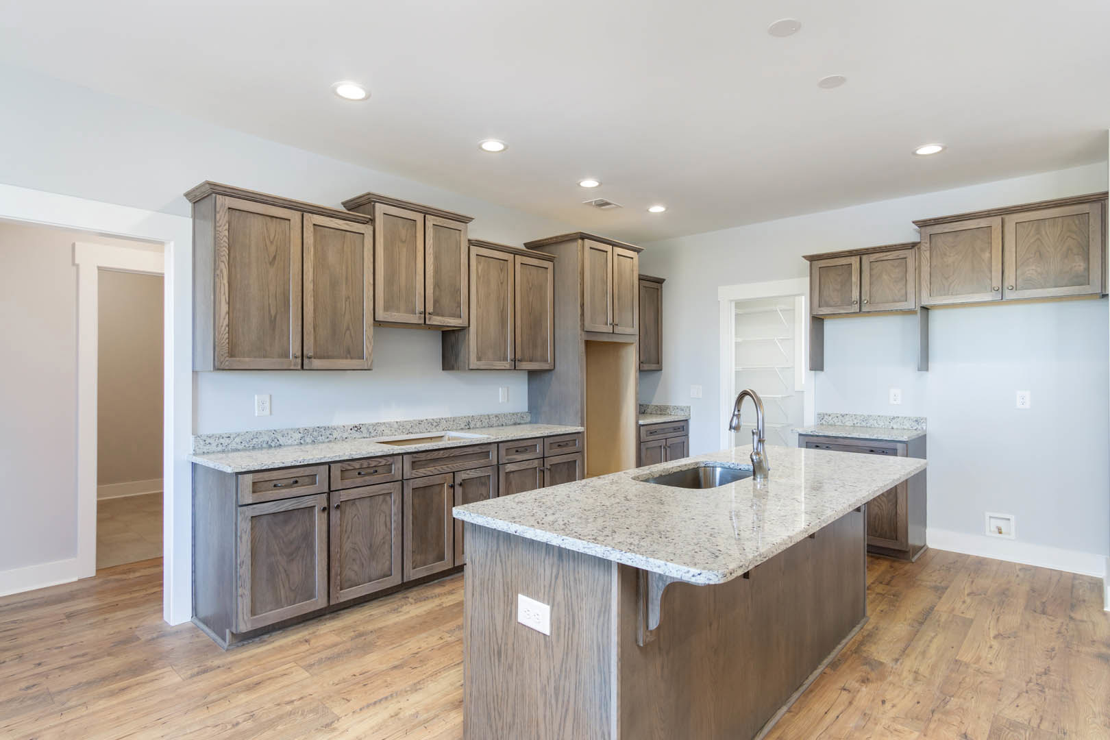 Spacious kitchen featuring a large wood island with granite countertops, built-in sink, white rectangular object on the surface, tile flooring, and surrounding cabinetry.