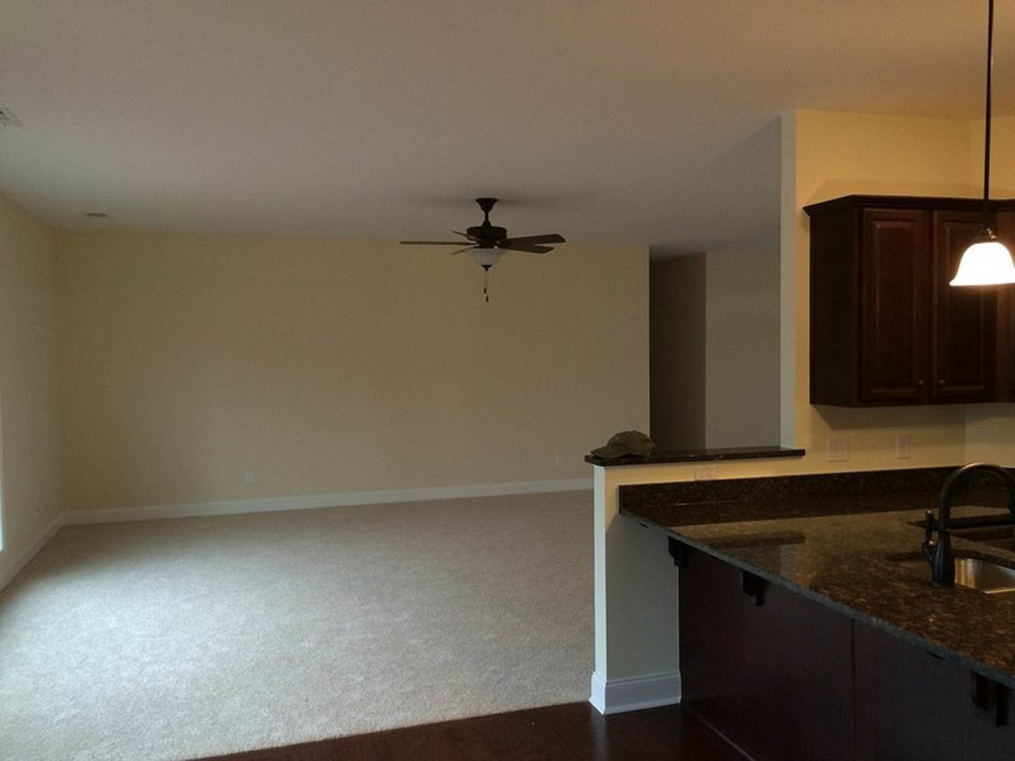 Modern kitchen with wood cabinetry, stone countertop, stainless steel sink and faucet, ceiling fan with integrated light, neutral walls, and tile flooring