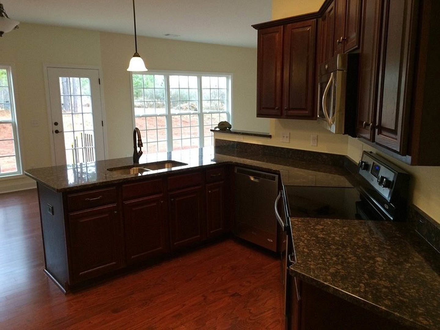 Kitchen with dark wood cabinets, speckled granite countertops, stainless steel appliances, large window, and close-up views of stove knobs and refrigerator handle