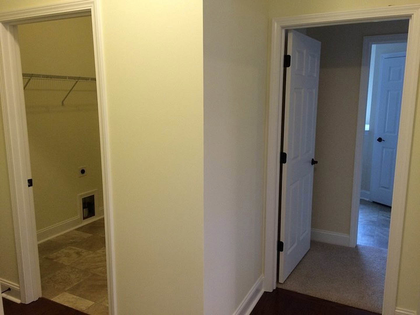 White closet door with matte black handle, open to reveal tile flooring and plaster walls in a modern room