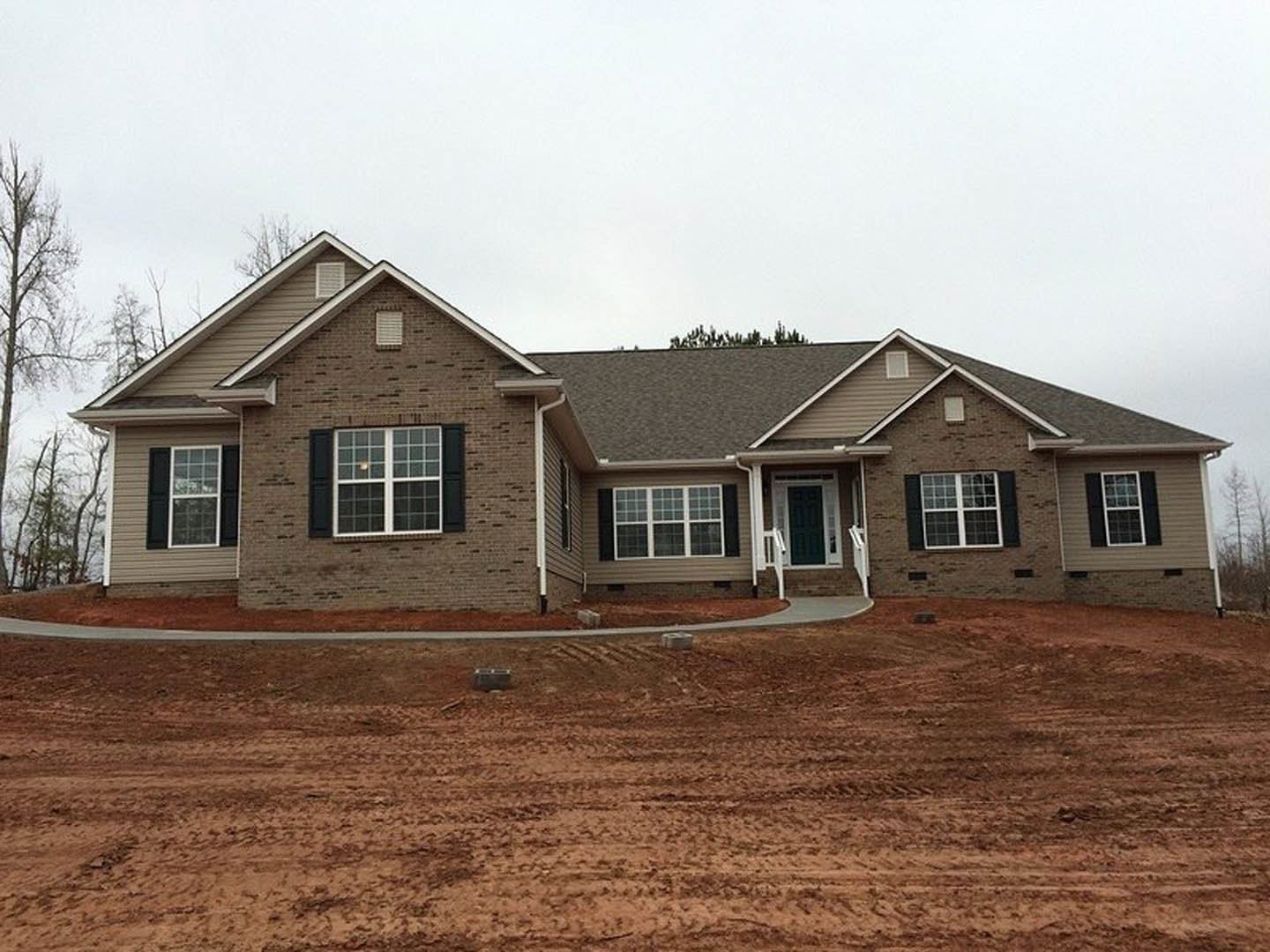 Two-story house with light siding, green front door, white-framed windows, and a dirt hill in the foreground