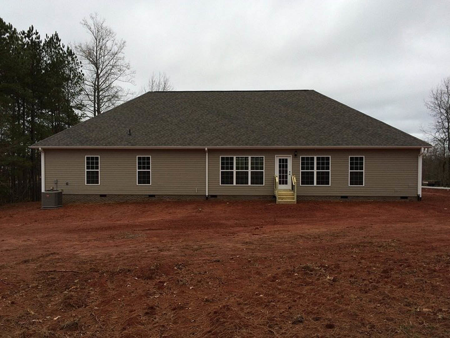 White house with multiple square-paned windows, white front door, and covered porch, set behind a dirt yard; trees and cloudy sky in background.