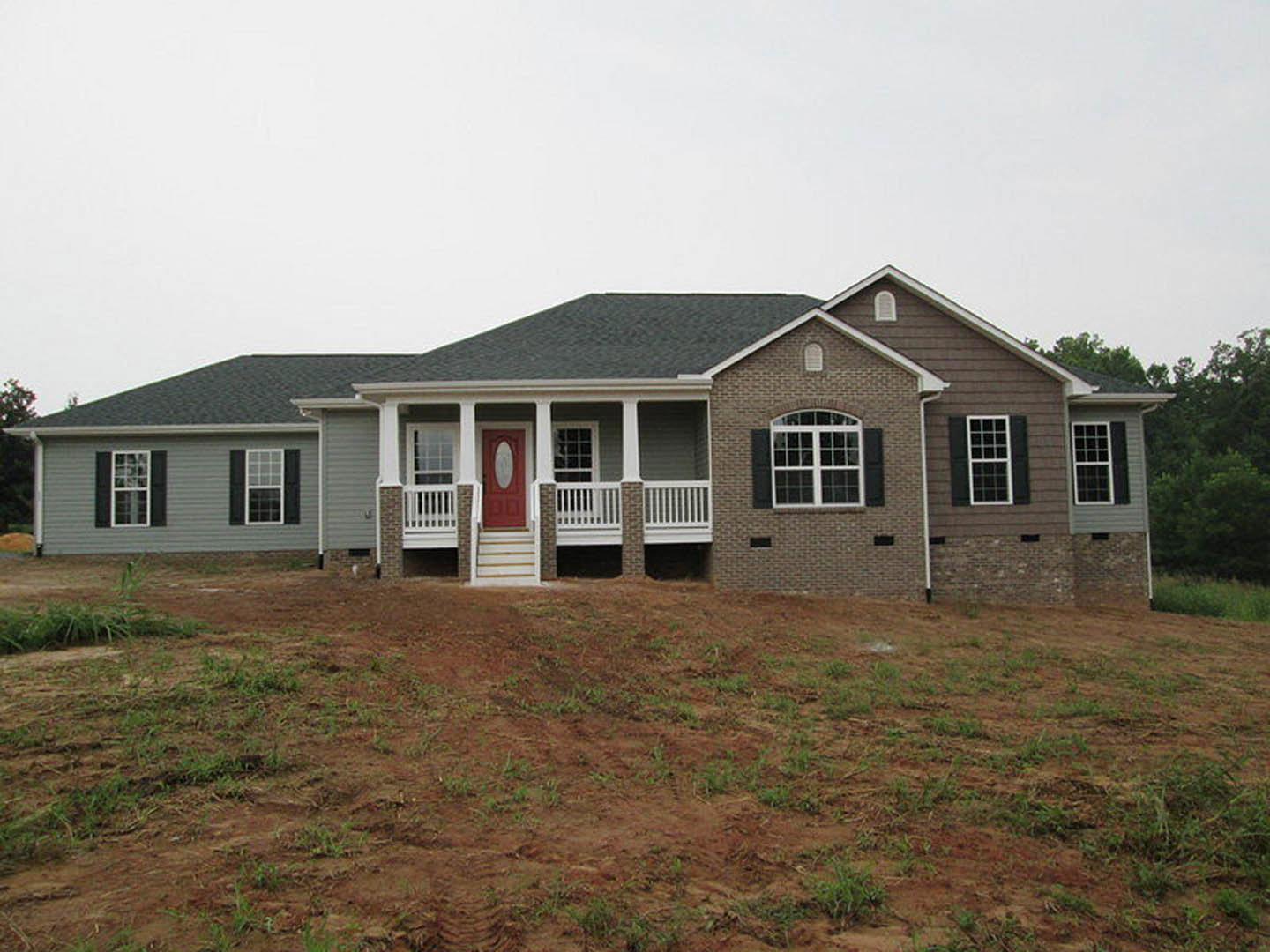 Red front door with oval glass inset, white multi-pane windows, light siding, grassy yard, and small porch under blue sky.