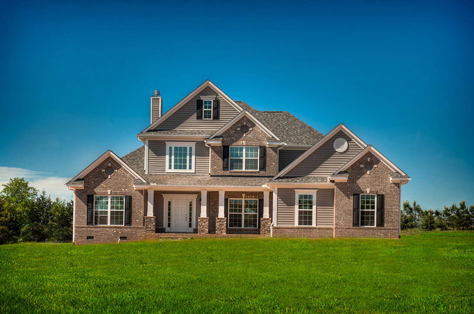 Two-story farmhouse with white siding, multi-pane windows, glass-paneled front door, covered porch, and manicured green lawn under a clear blue sky