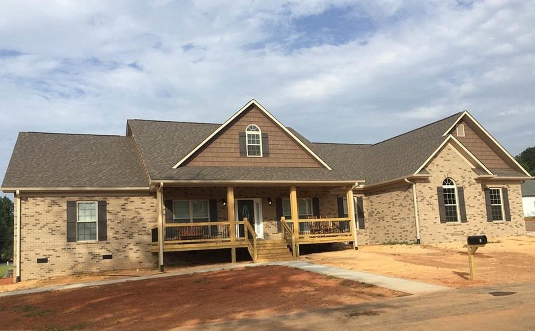 Two-story home with white siding, multi-pane windows, wooden porch with railing, and paved driveway under partly cloudy sky