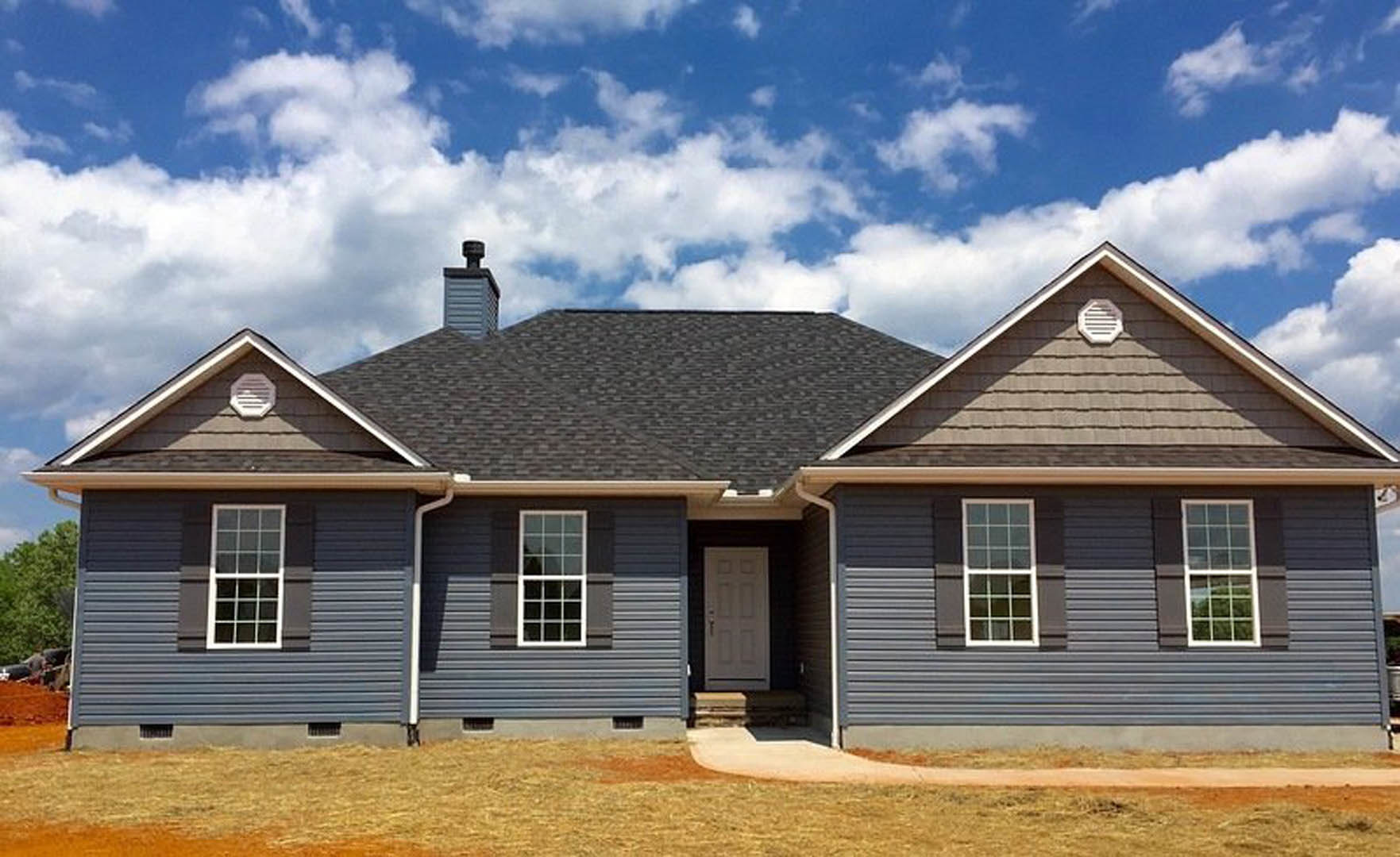 Blue metal roof with white siding, black-framed front door, multi-pane windows, white roof vent, and cloudy sky background