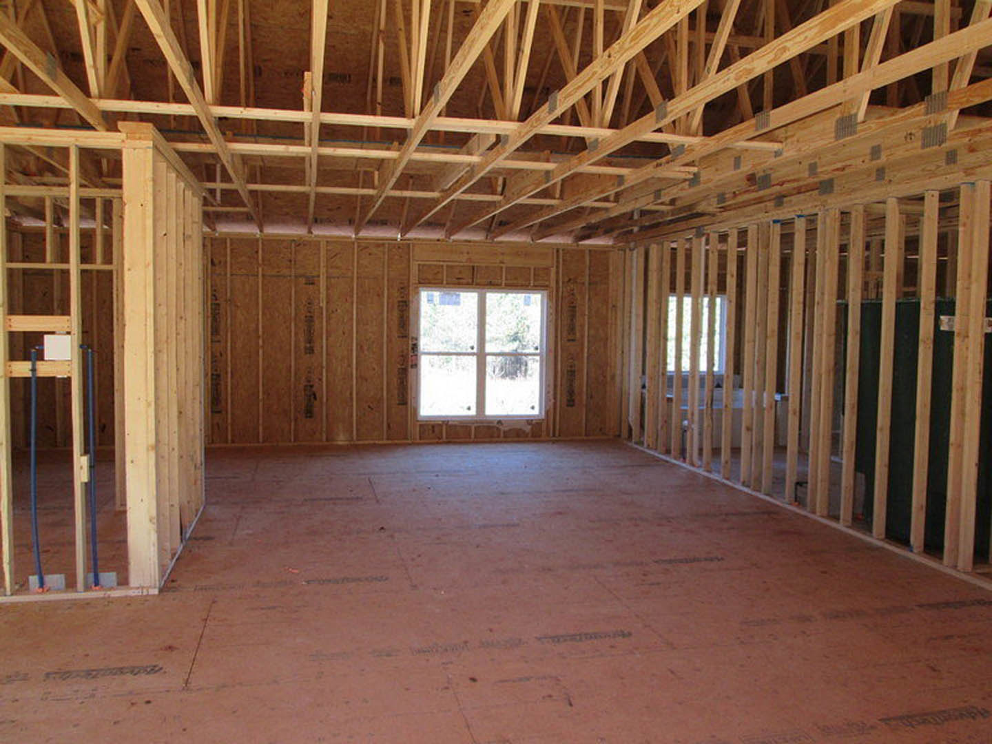 Living room with exposed wood ceiling beams, white-framed window, light hardwood floors, and neutral walls