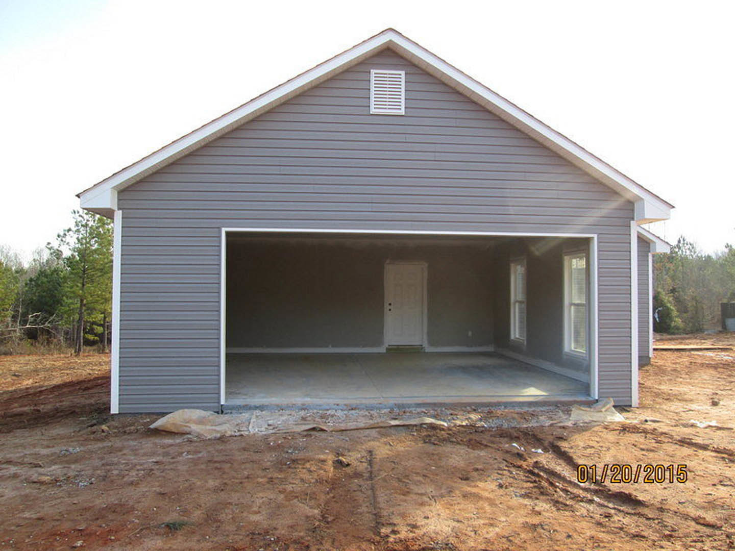 Garage under construction featuring a white paneled door, brick wall with white vent, and dirt ground in front