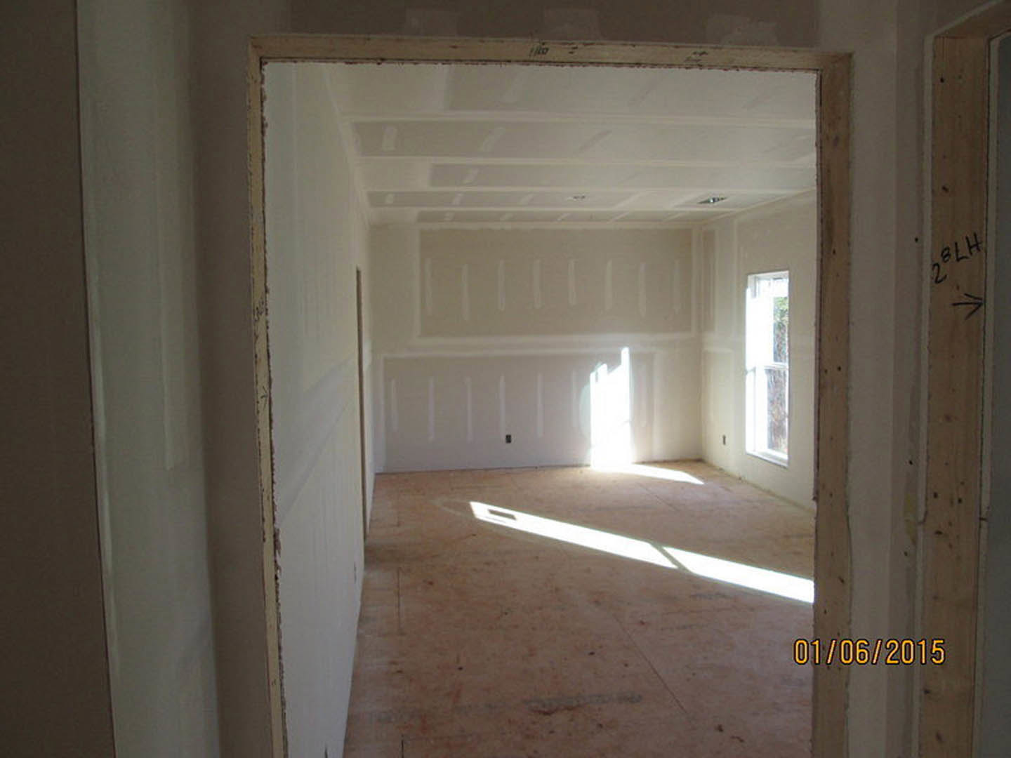White-walled room with open door, sunlight streaming through window onto light wood floor, simple ceiling molding, and yellow house number visible