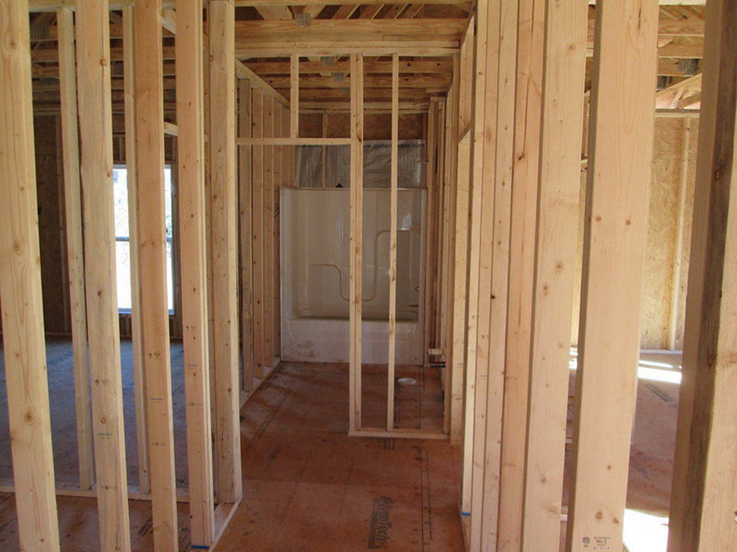 Bathroom under construction with exposed wood framing, plywood subfloor, and partially installed shower enclosure