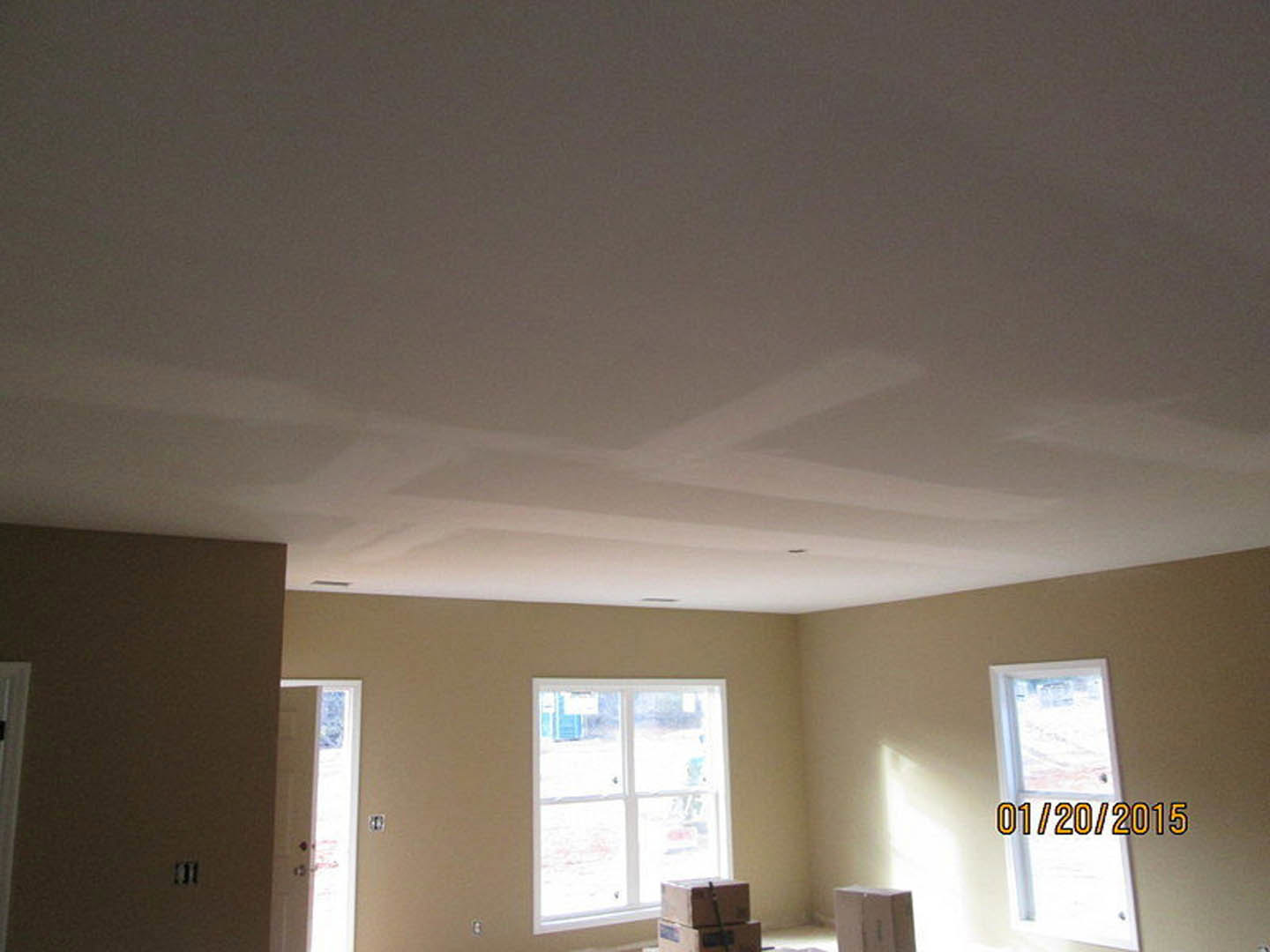 Unfinished room with stacked cardboard boxes on hardwood floor, white plaster walls, large window, and white ceiling with ceiling fan fixture