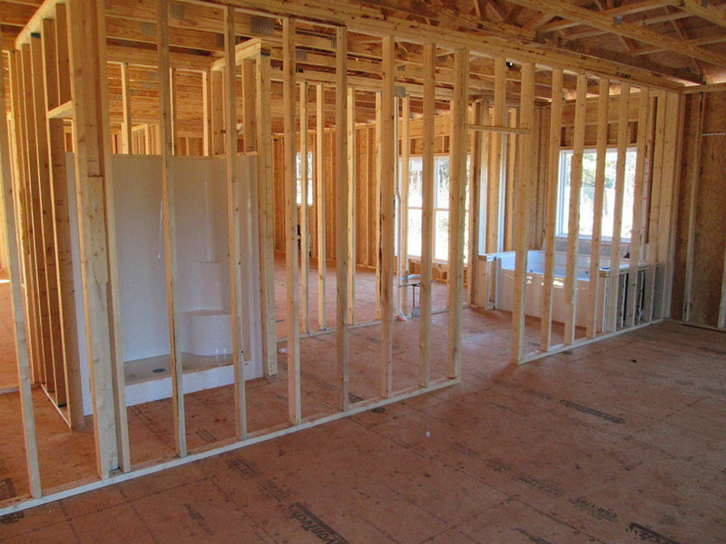 Bathroom under construction with exposed wood framing, unfinished walls, bathtub installed, visible ceiling beams, and construction materials scattered on subfloor.