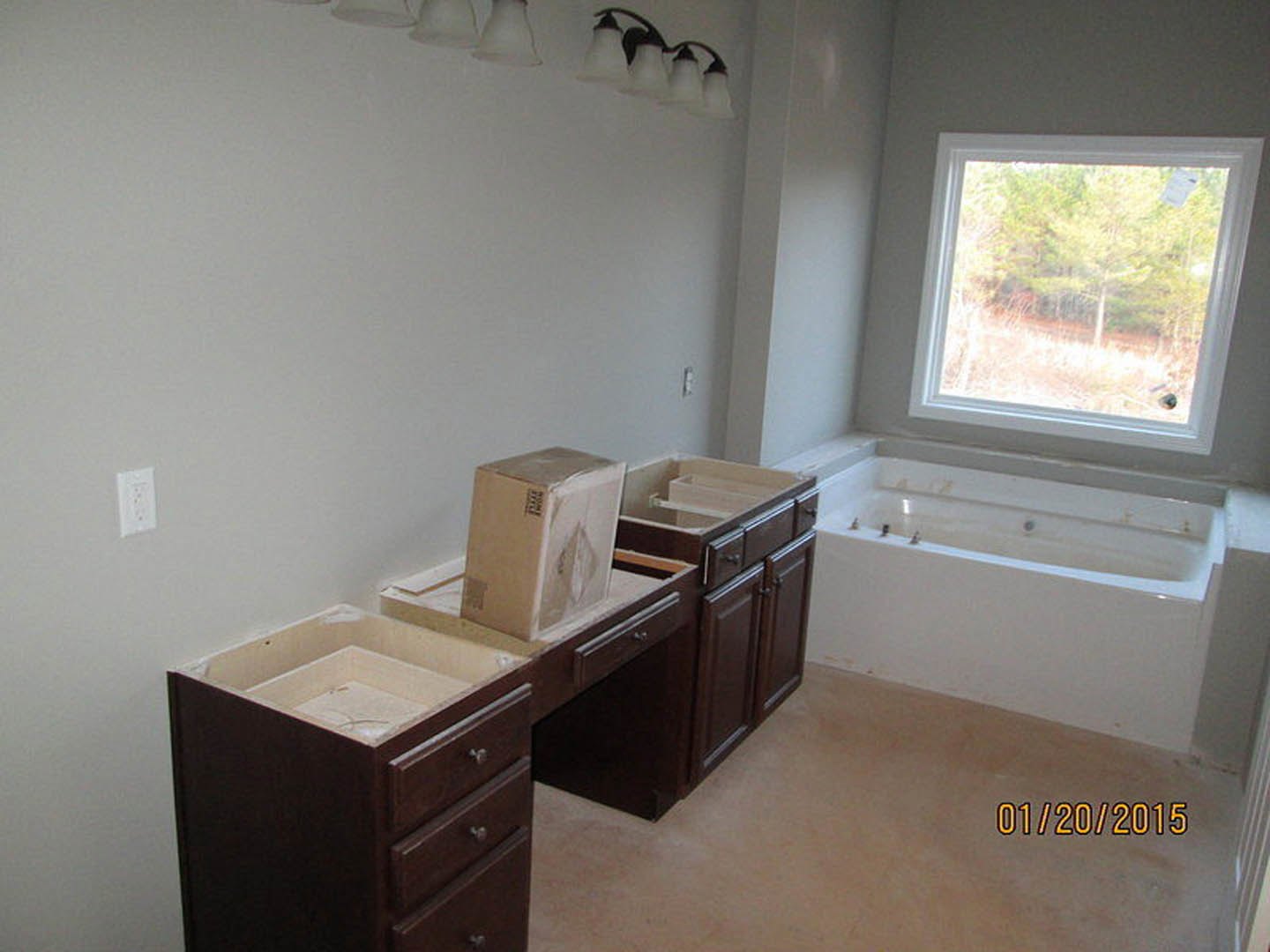 Bathroom featuring a freestanding bathtub beneath a window with trees visible outside, white countertop with cabinetry and drawers, wall-mounted electrical outlet, and modern light