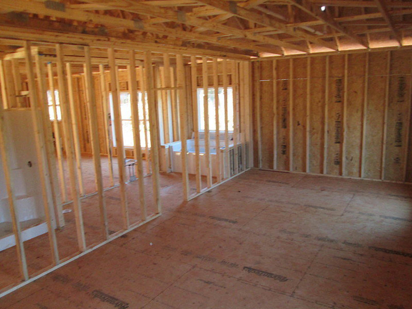 unfinished room with exposed wood framing, ceiling beams, and wall studs, plywood subfloor, insulation visible between studs