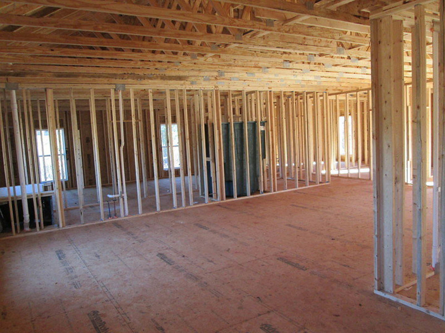 Open room featuring exposed wood ceiling beams, metal tank against a wooden wall, plank flooring, and a window providing natural light