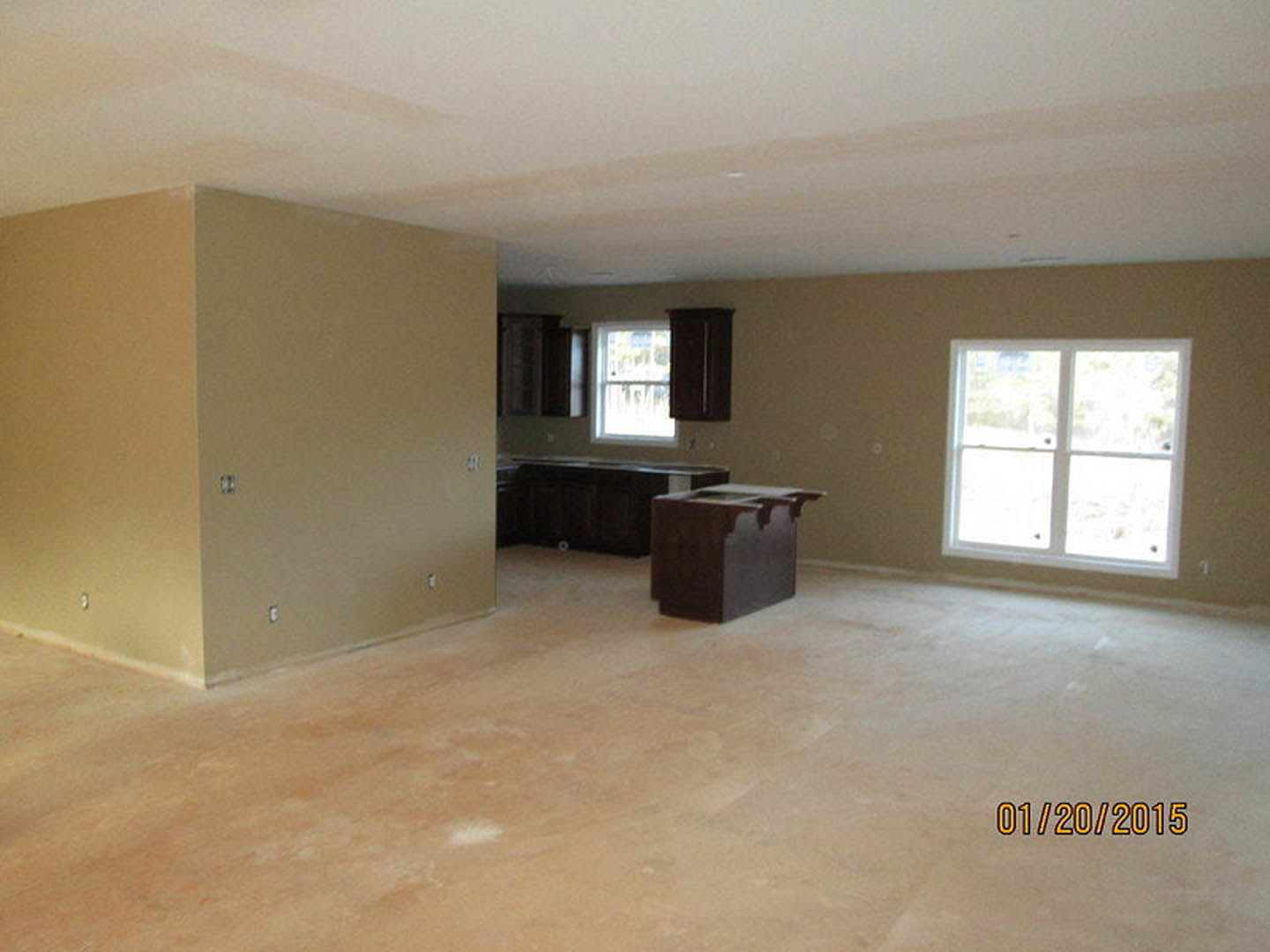 Open-concept kitchen with white cabinetry, laminate flooring, wood dining table, white-framed window, and a person seated at the table