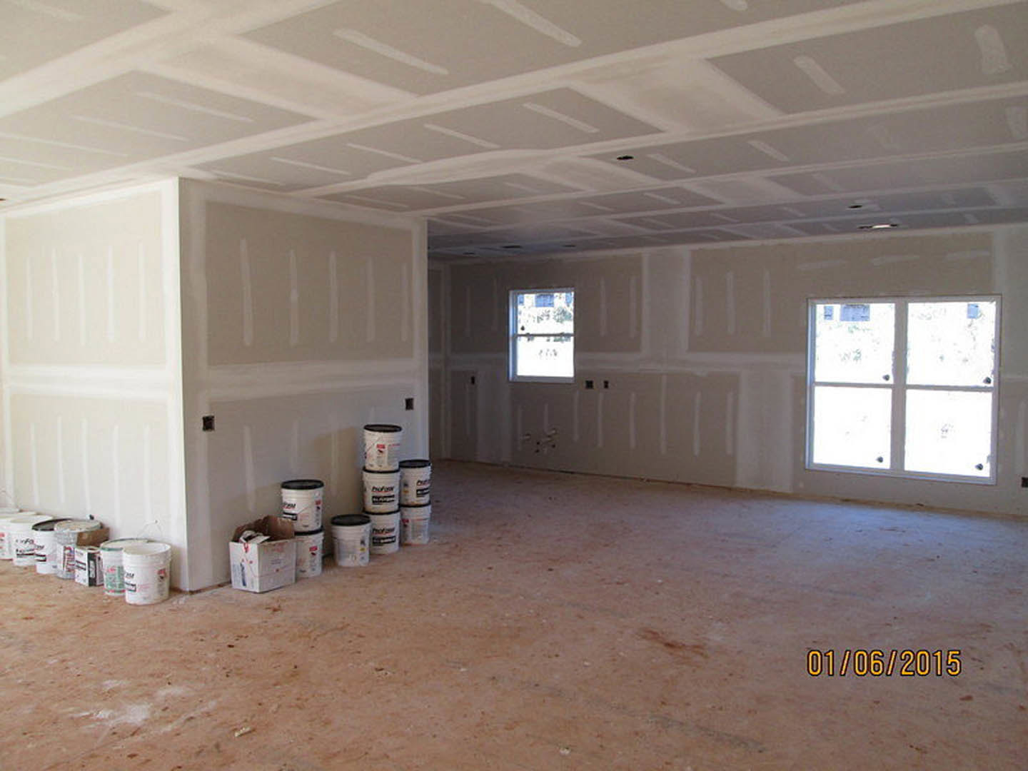 White-walled room with several paint buckets stacked on the floor, large windows with white frames, and smooth plaster ceiling and flooring.