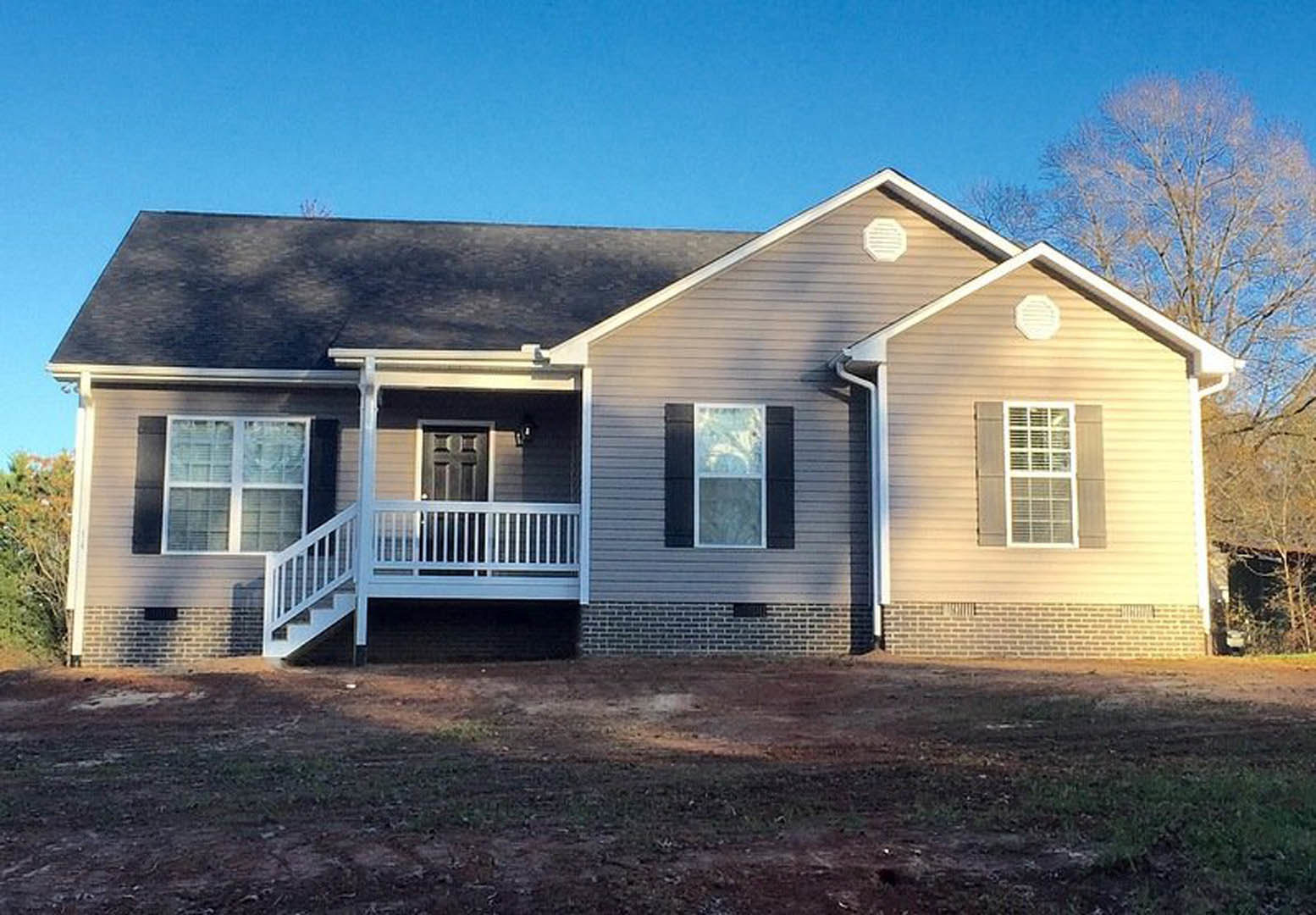 Two-story house with light siding, covered front porch, white framed windows, landscaped green yard, and mature trees in the background