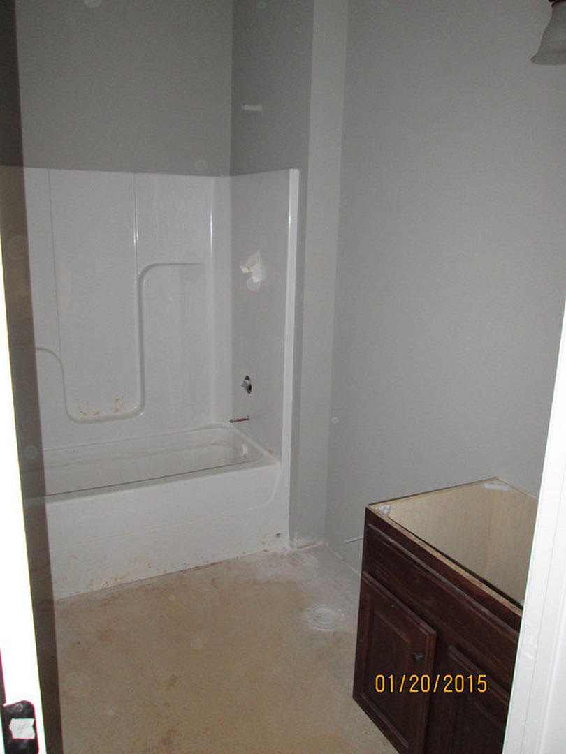 Bathroom with freestanding white tub, rectangular sink on wood vanity, light tile floor, white plaster walls, and built-in cabinetry
