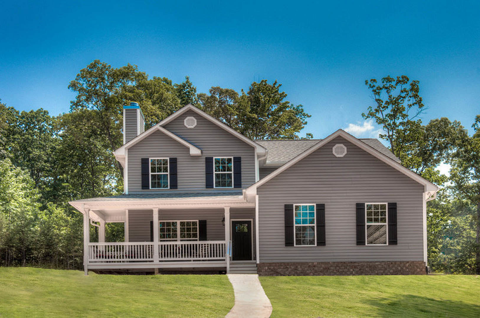 Two-story house with covered porch, white railing, black front door with window, blue glass window panes, concrete walkway, green lawn, and trees in background