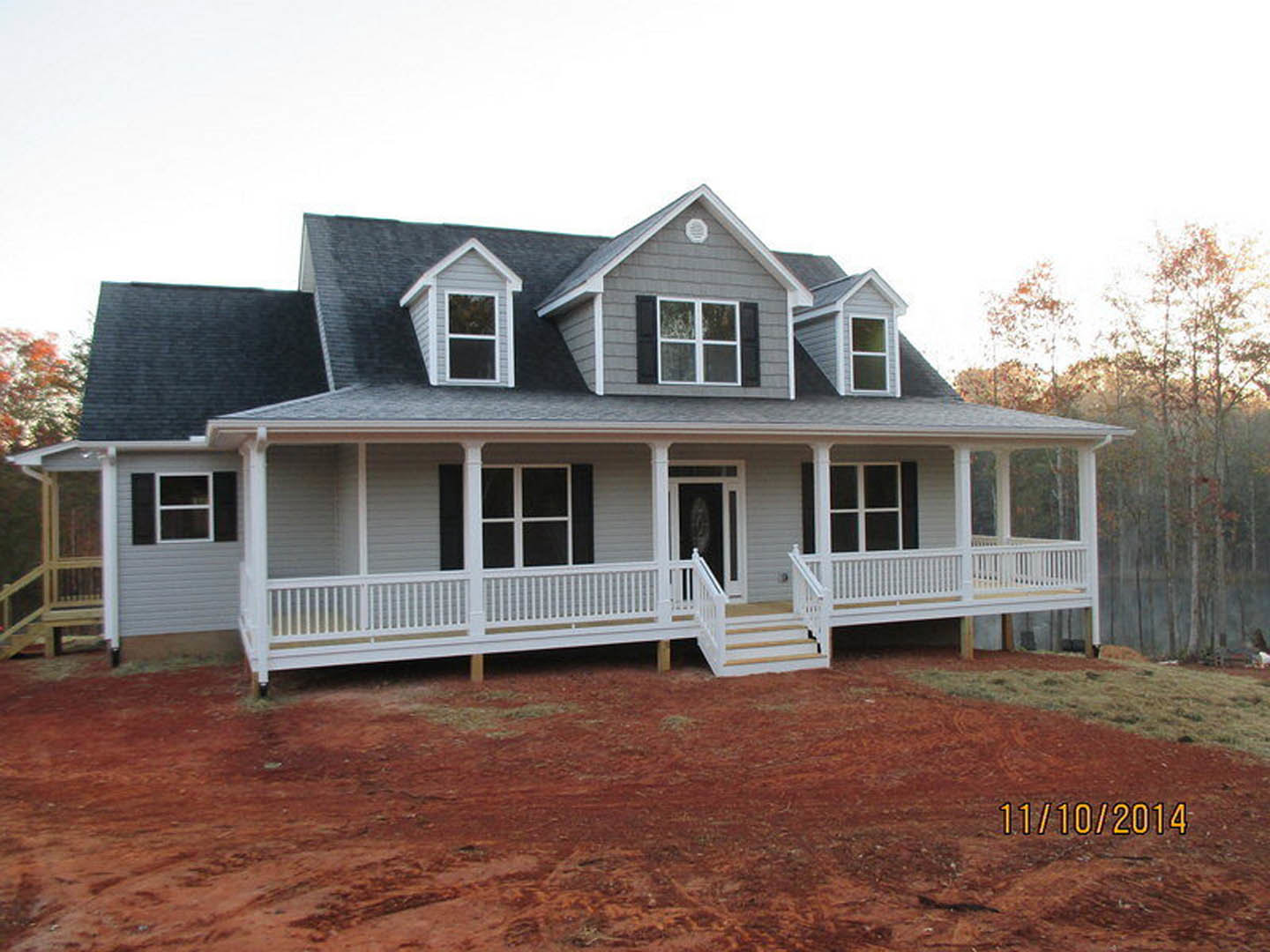 White porch with stairs and railing, large window, red dirt yard, light-colored siding, tree in background
