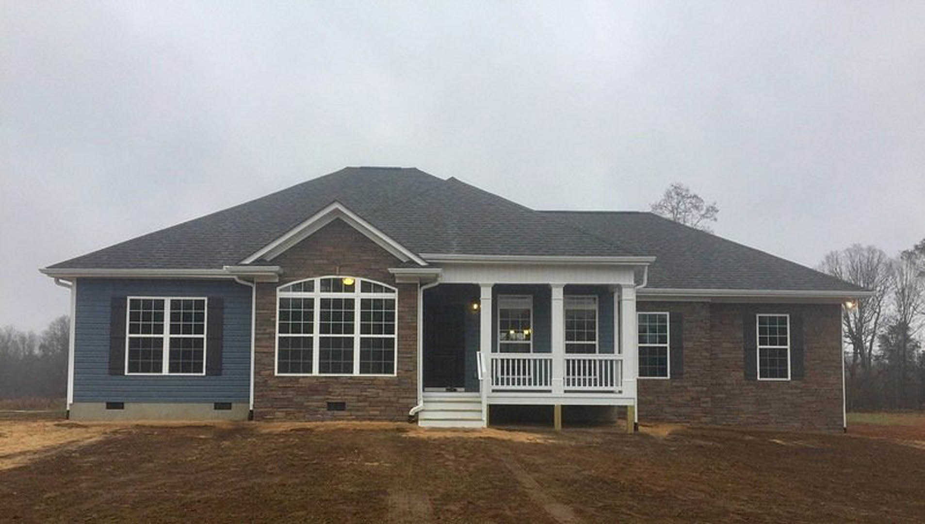 Two-story house with white porch railings, multiple windows, and trees in the background under a partly cloudy sky