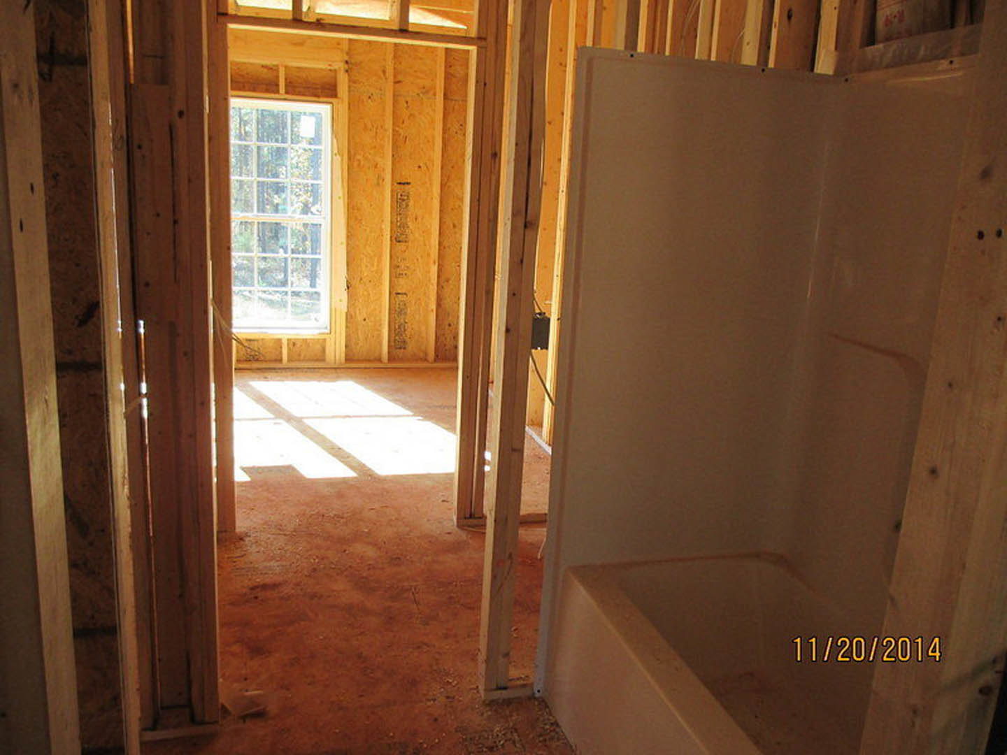 Bathroom under construction with exposed wood framing, plaster walls, freestanding tub, sink, and multi-pane window letting in natural light onto unfinished floor.