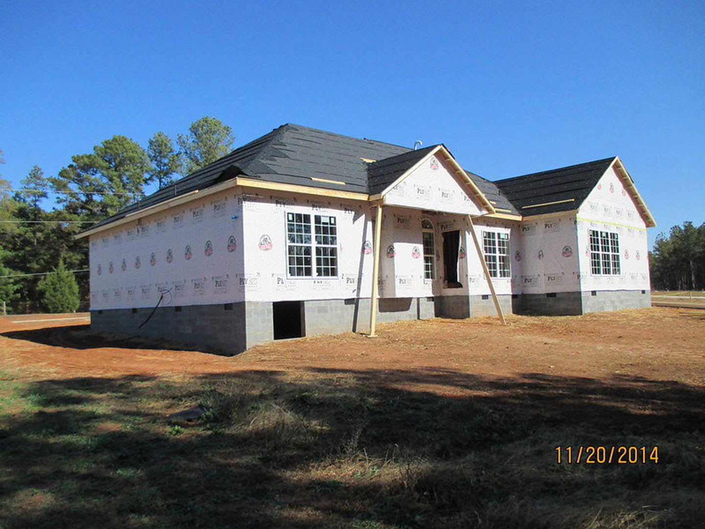 Two-story house under construction with black roof, white walls, large windows, patch of dirt in front yard, and construction sign in the middle of the property