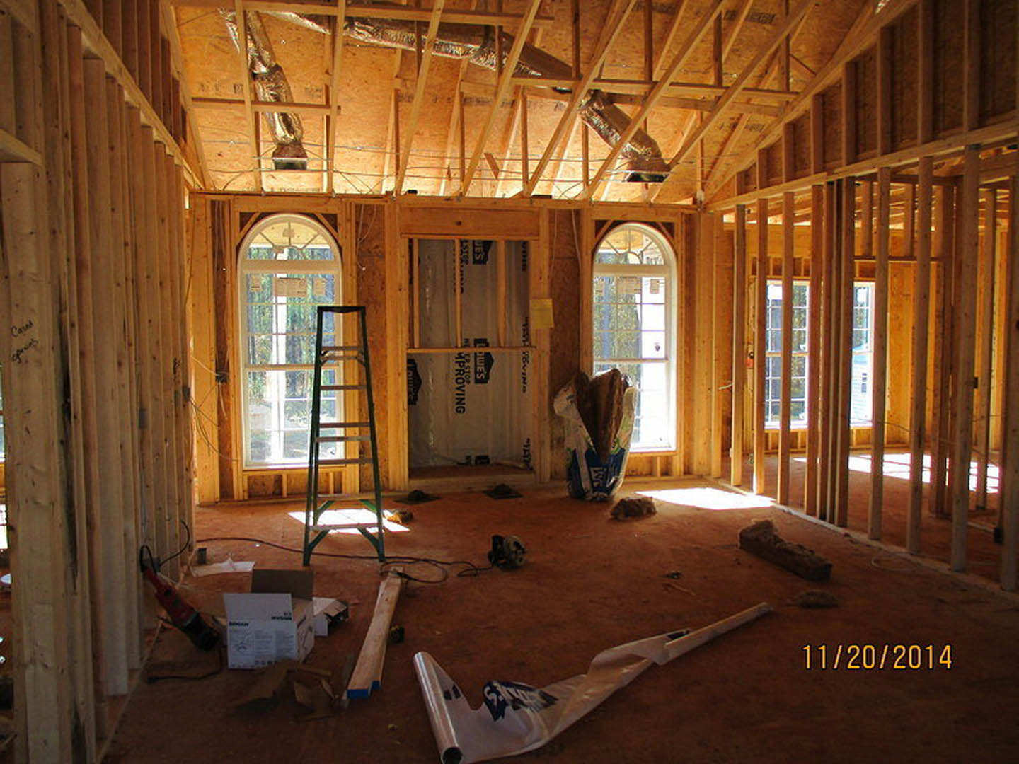 Open room with exposed wood beams, tall ceiling, two ladders, plastic bag on floor, large windows, white walls, natural daylight