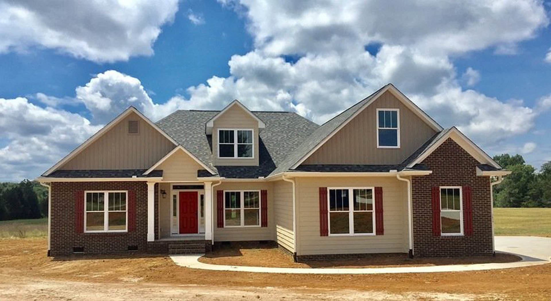 Red front door with white trim on a cottage-style home, white-framed window, gray shingle roof, partly cloudy sky in background