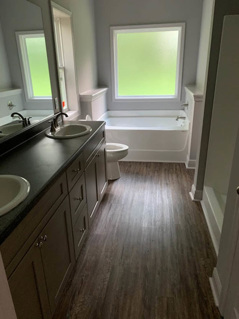 Bathroom with wood plank flooring, large window, freestanding bathtub, white porcelain sink, and modern toilet