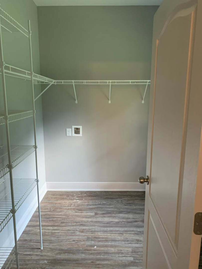 Walk-in closet with white shelving, wood plank flooring, white walls, ceiling light fixture, and a framed square picture on the wall