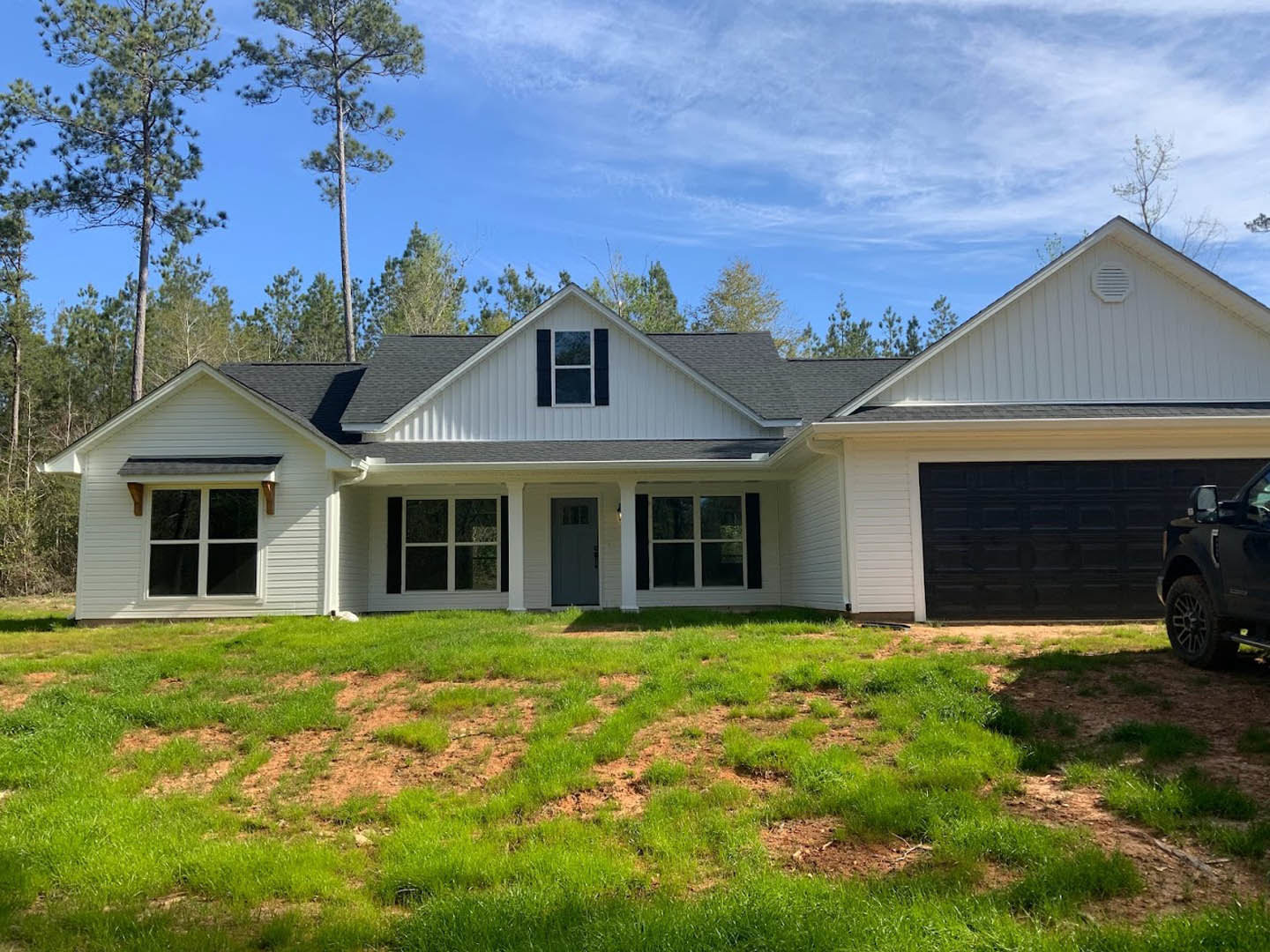 Two-story house with grey front door, white siding, large windows, and green lawn bordered by mature trees
