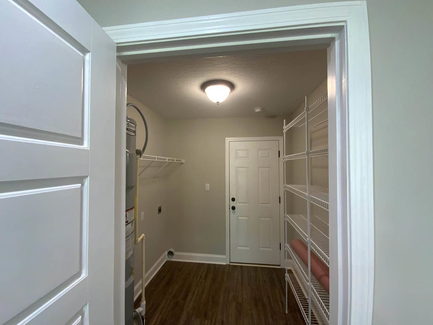 Walk-in closet with white built-in shelves, white door with black knobs, wood flooring and white baseboard trim, ceiling light fixture