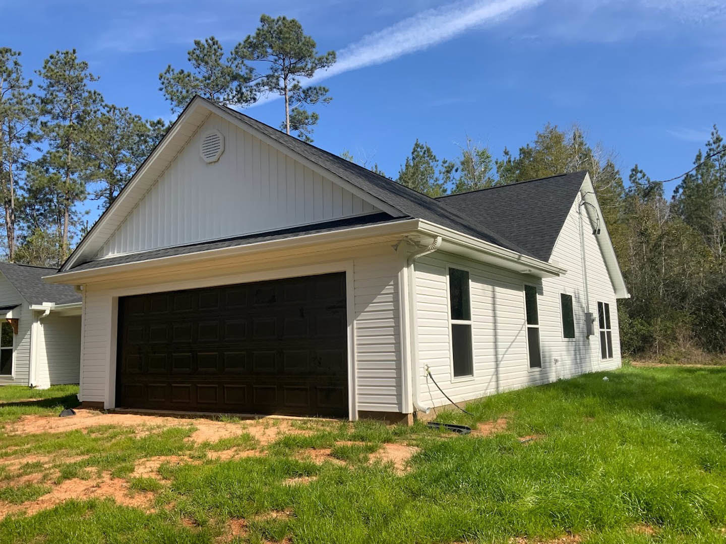 White house with black garage door and white trim, vent above garage, grassy front yard, window on side, American Gothic House visible in background, trees and cloudy sky