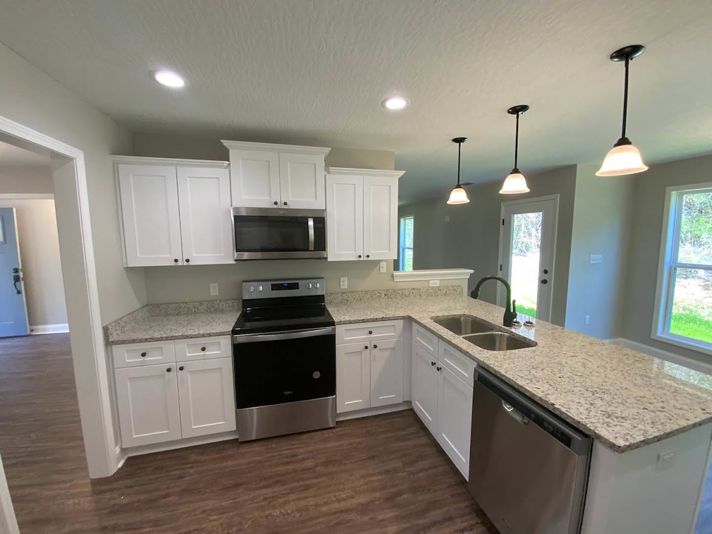 White kitchen cabinets and granite countertops with stainless steel dishwasher, built-in microwave, black faucet, white-framed window, and undermount sink.