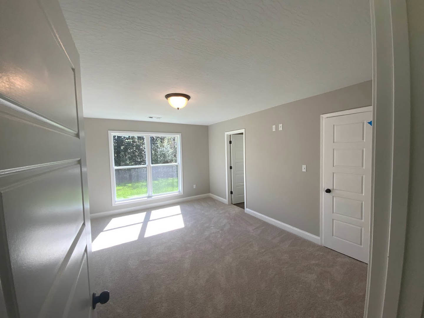 White door with black handle and hinges, white-framed window, light fixture on ceiling, smooth plaster walls, light-colored flooring