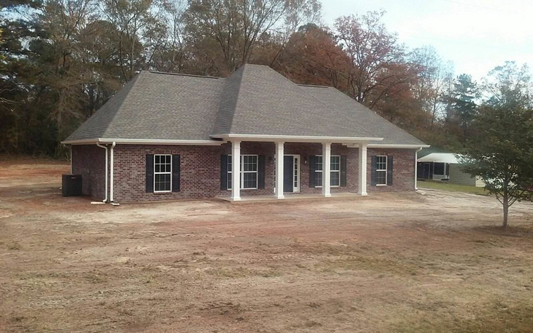 Red brick house with white columned porch, silver door handle, white-framed windows, tree in front, dirt yard