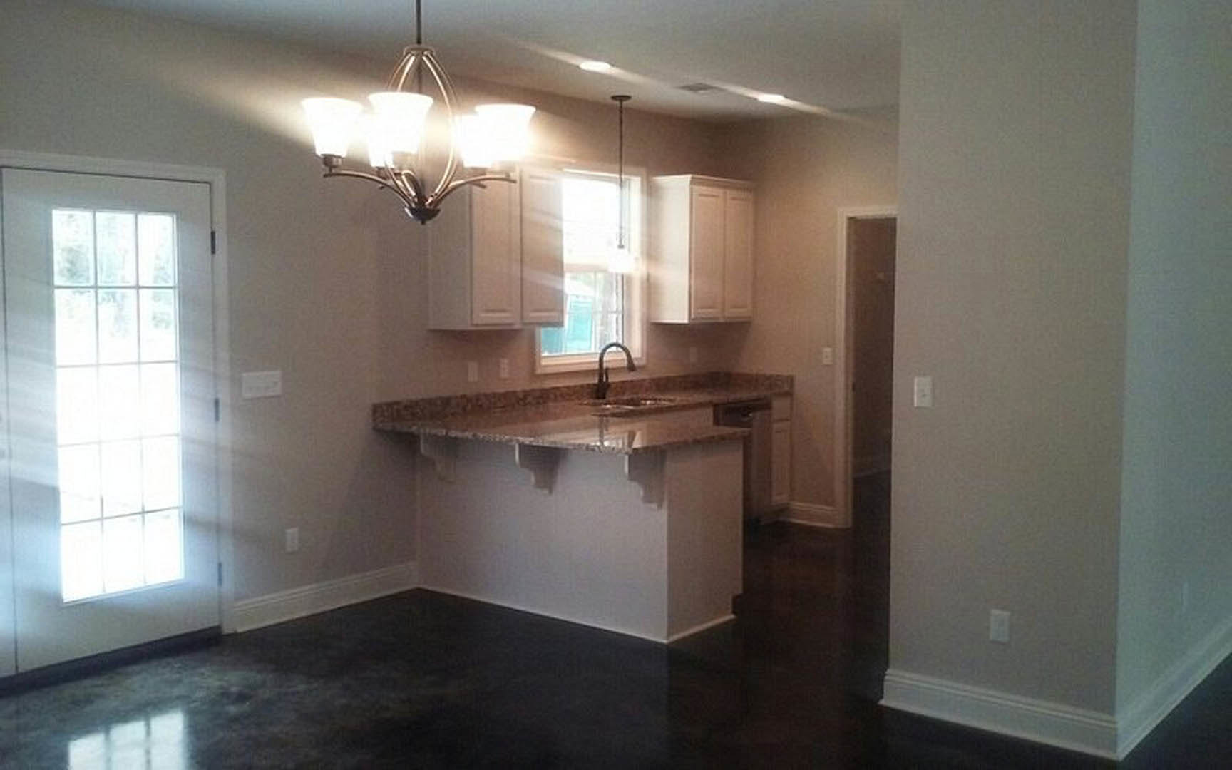 Modern kitchen featuring tile flooring, white cabinetry, stone countertops, stainless steel sink, and a contemporary chandelier suspended from the ceiling.