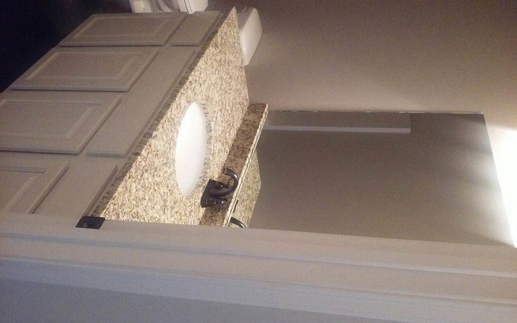 White porcelain sink set into a light-colored countertop with a sleek cabinet below, against a smooth white wall and ceiling in a modern bathroom.