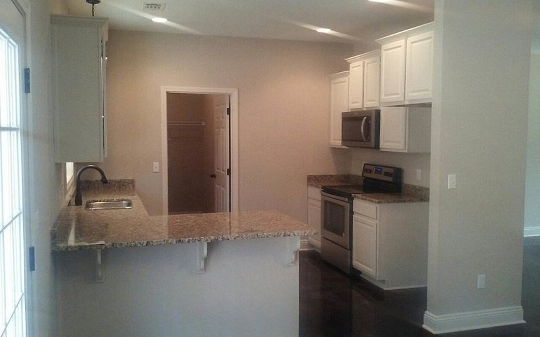 Granite countertops and white cabinets in a kitchen with tile flooring, stainless steel stove and microwave, open closet door, sink, and blurred window and table in the background