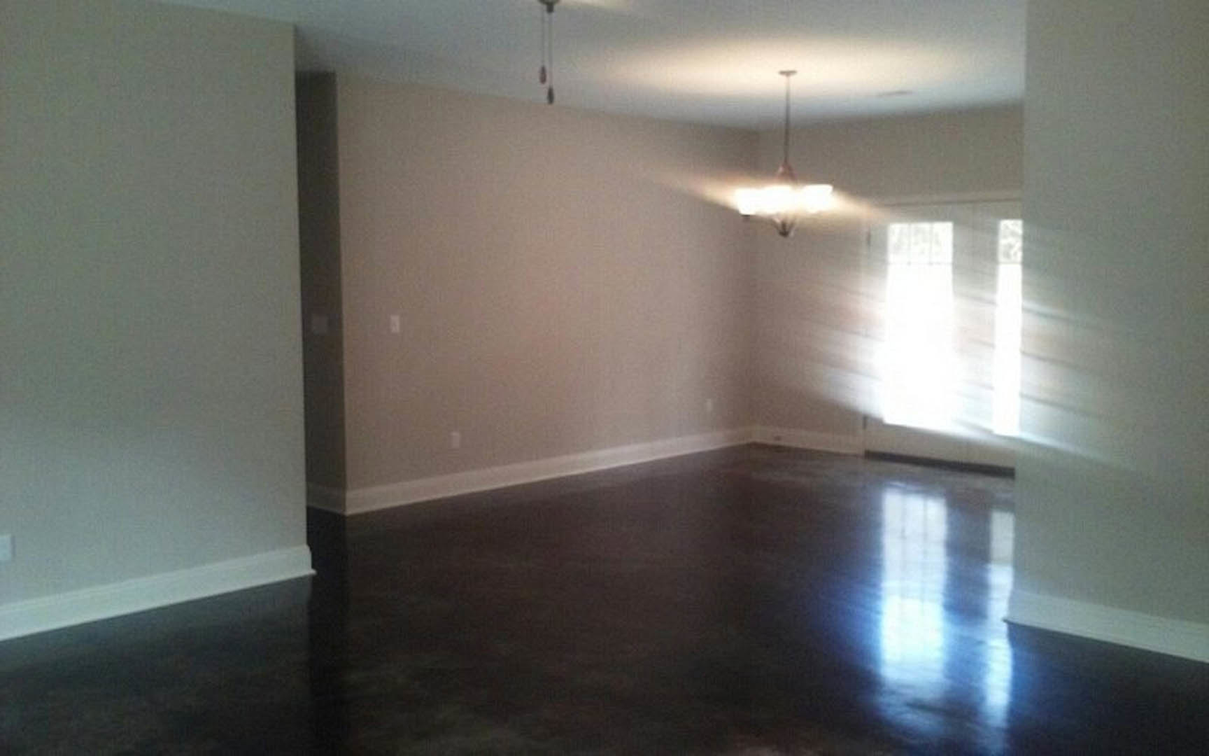 Sunlight streaming through a window onto dark wood flooring, white walls with black trim, and a blurred chandelier overhead