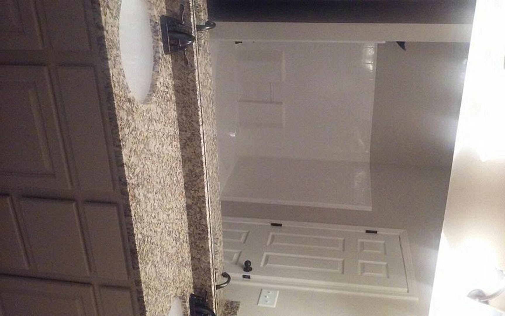 White bathroom with a rectangular sink, white paneled door featuring a black handle, white outlet on plaster wall, and a sheer white curtain.